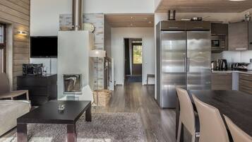 A modern kitchen with stainless steel appliances, a dining area with a table and chairs, and a living room with a sofa and a fireplace.