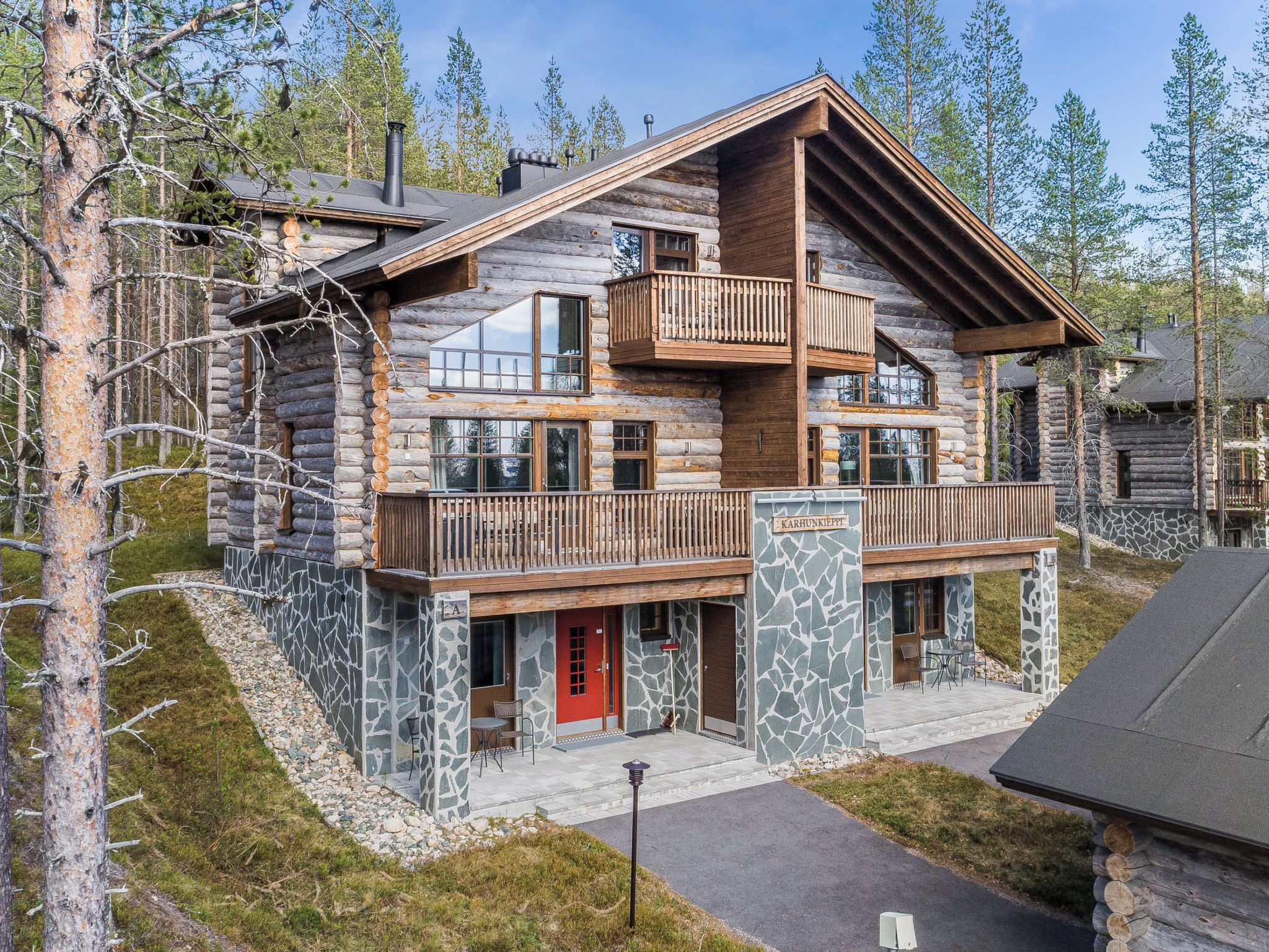 A log cabin with a stone foundation, a red door, and a balcony.