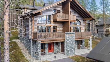 A log cabin with a stone foundation, a red door, and a balcony.