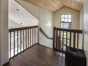 A spacious balcony with a wooden railing, a staircase leading to an upper level, and a view of the outside.