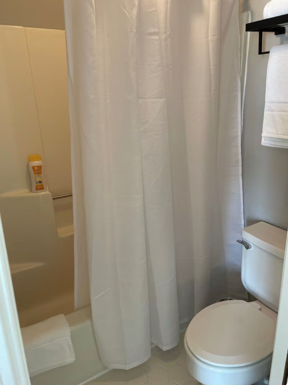A bathroom with a shower, toilet, and a bottle of shampoo on the floor.