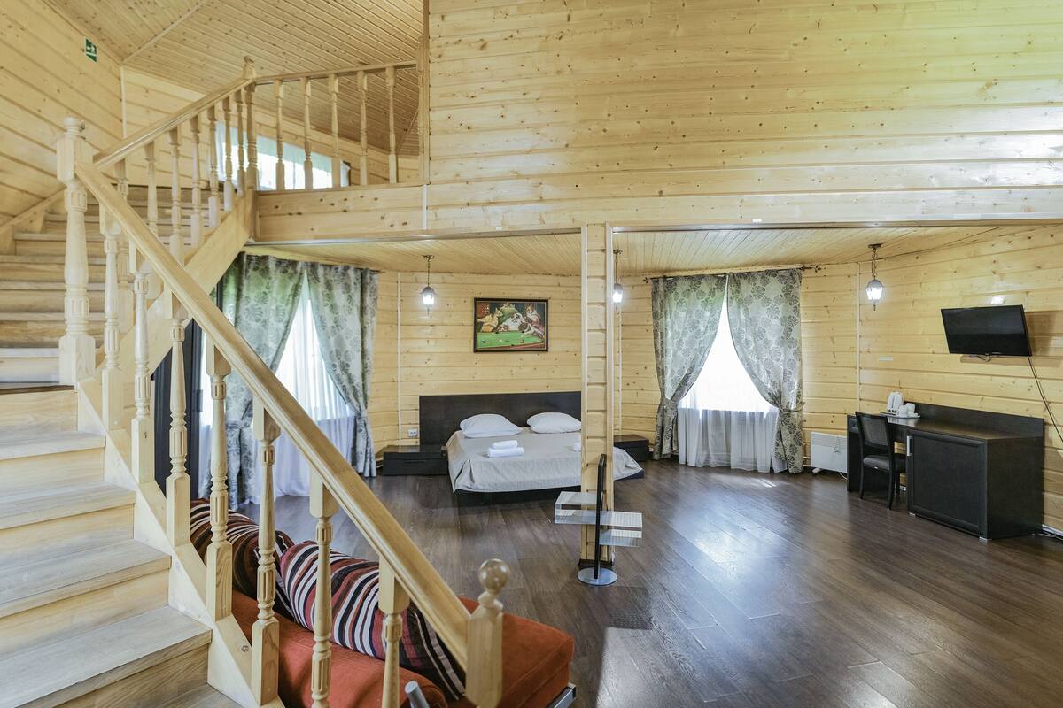 A wooden cabin interior with a staircase, a bed, a desk, and a television.