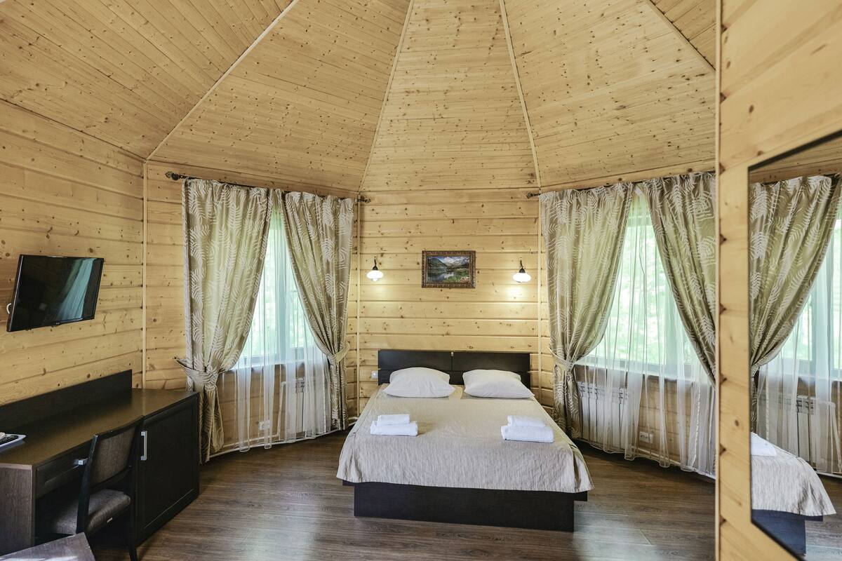 A wooden cabin bedroom with a bed, a desk, and a TV.