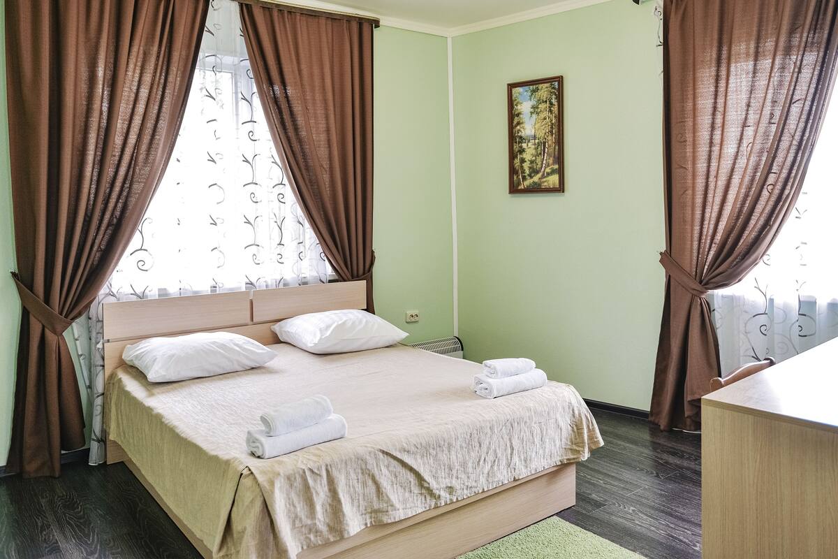 A neatly made bed with white linens and towels, a wooden headboard, and brown curtains.