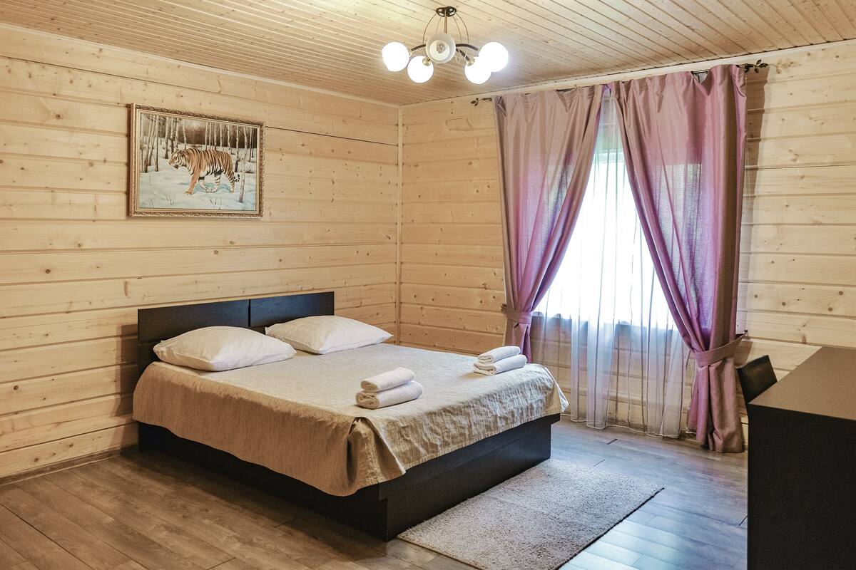 A wooden-paneled room with a bed, a painting of a tiger, and a window with purple curtains.