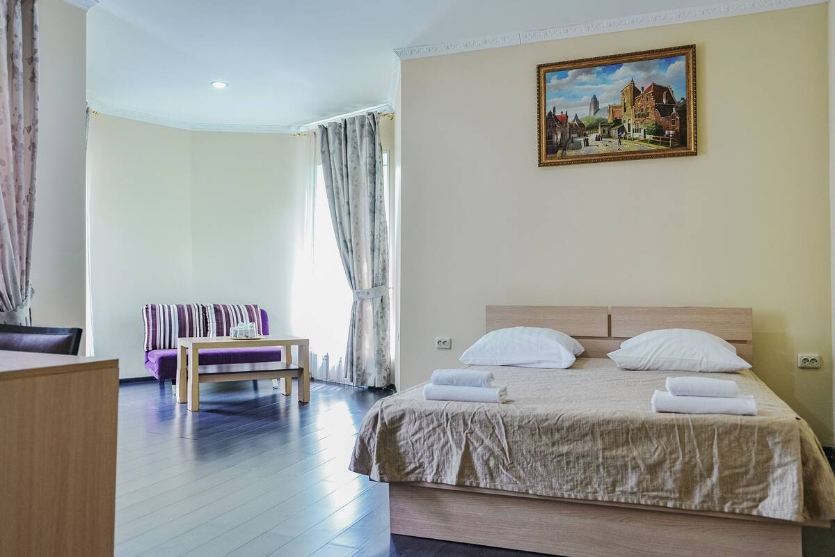 A hotel room with a bed, a sofa, a table, and a painting on the wall.