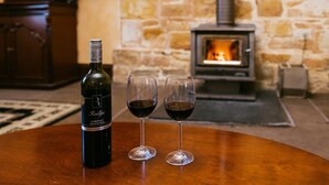 Reillys-tuotemerkin vuoden 2017 Cabernet Sauvignon -viinipullo ja kaksi viinilasia puisella pöydällä kiviseinän ja puukamin edessä.