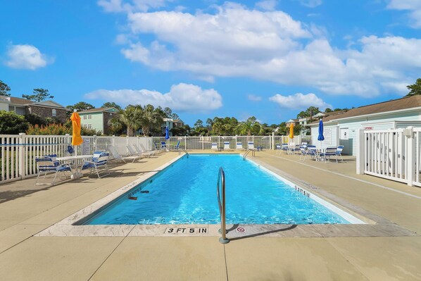 A rectangular swimming pool with a 3 ft 5 in depth marker, surrounded by white fences, blue lounge chairs, and umbrellas.