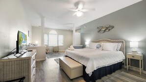 A spacious bedroom with a large bed, a desk with a computer, a chair, and a window with a view. - Book your Sea Trail getaway in this ground floor, pet friendly condo (Sunset Beach)