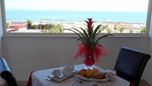A table with a newspaper, a cup, a plate with fruit, and a decorative vase. - Hotel Belvedere (Margherita di Savoia)
