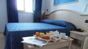 A hotel room with a bed, a bedside table with breakfast items, a nightstand, and a window with curtains. - Hotel Belvedere (Margherita di Savoia)