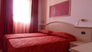 Una camera d'albergo con due letti, un comodino, uno specchio e una finestra con tende.
