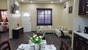 A compact living space with a dining area, a sofa, a kitchen, and a door leading to another room.