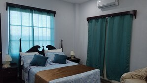 A bedroom with a bed, two bedside tables, a lamp, a chair, and a window with curtains.