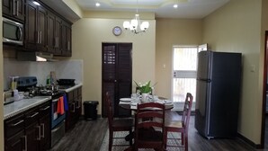 A kitchen with dark wooden cabinets, a microwave, a stove, and a refrigerator. There is a dining table with chairs and a chandelier above.