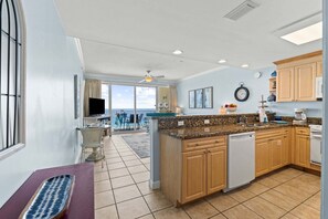 A kitchen with a large island, wooden cabinets, a dishwasher, and a view to the outside.