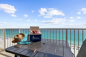 A balcony with a view of the ocean, a table with a hat and a cooler, and a striped towel.