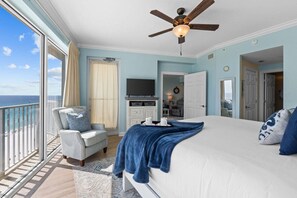 A bedroom with a bed, a chair, a TV, and a balcony with a view of the ocean.