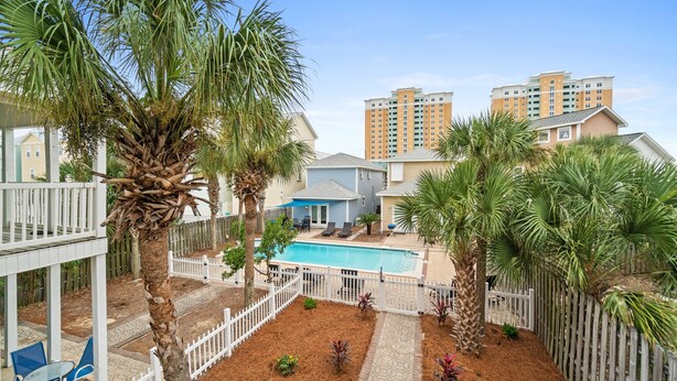 A pool area with palm trees, a fenced deck, and a view of high-rise buildings in the background.