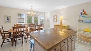 A kitchen with a granite island, wooden chairs, a chandelier, and a sailboat decoration.