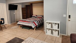 A bedroom with a bed, a wardrobe, a TV, a desk, and storage bins. - Centrally Located Mesa Studio (Mesa)