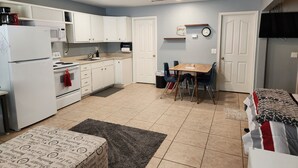 A compact kitchen with white cabinets, a microwave, and a stove. There is a dining table with chairs and a rug in the center. - Centrally Located Mesa Studio (Mesa)