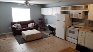 A compact living space with a kitchenette, a brown leather sofa, a wooden dining table, and a ceiling fan. - Centrally Located Mesa Studio (Mesa)