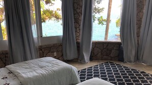 Ein Zimmer mit zwei Betten, einer Steinwand und Meerblick.