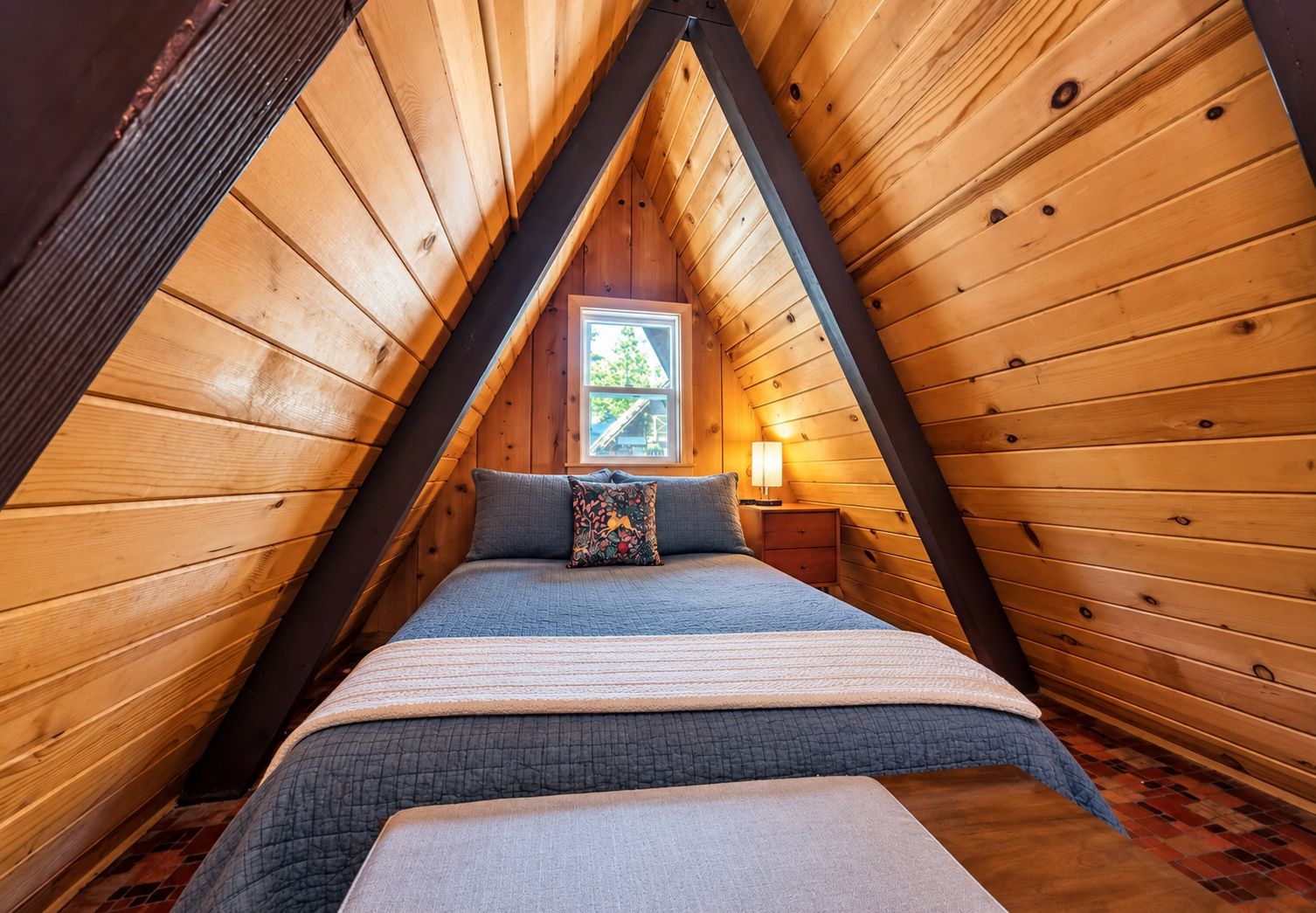 Un dormitorio con techo inclinado, una cama, una mesita de noche y un ventanal.