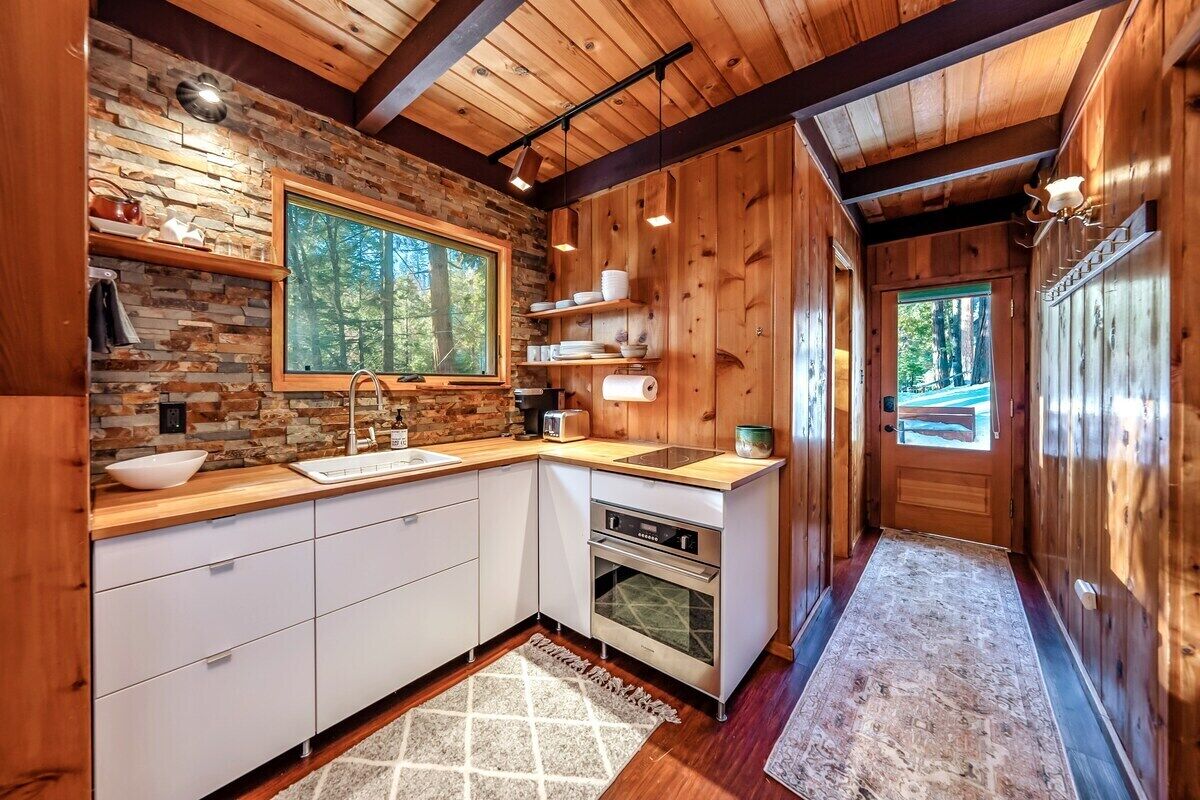 A modern kitchen with a stone wall backsplash, wooden cabinets, and a large window.