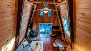 A cozy cabin interior with a loft bed, a dining area, and a fireplace.