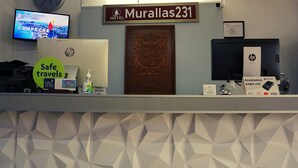 Una recepción de hotel con un letrero que indica Hotel Murallas 231, una computadora, una caja fuerte y un cartel que dice 'Buen viaje'.