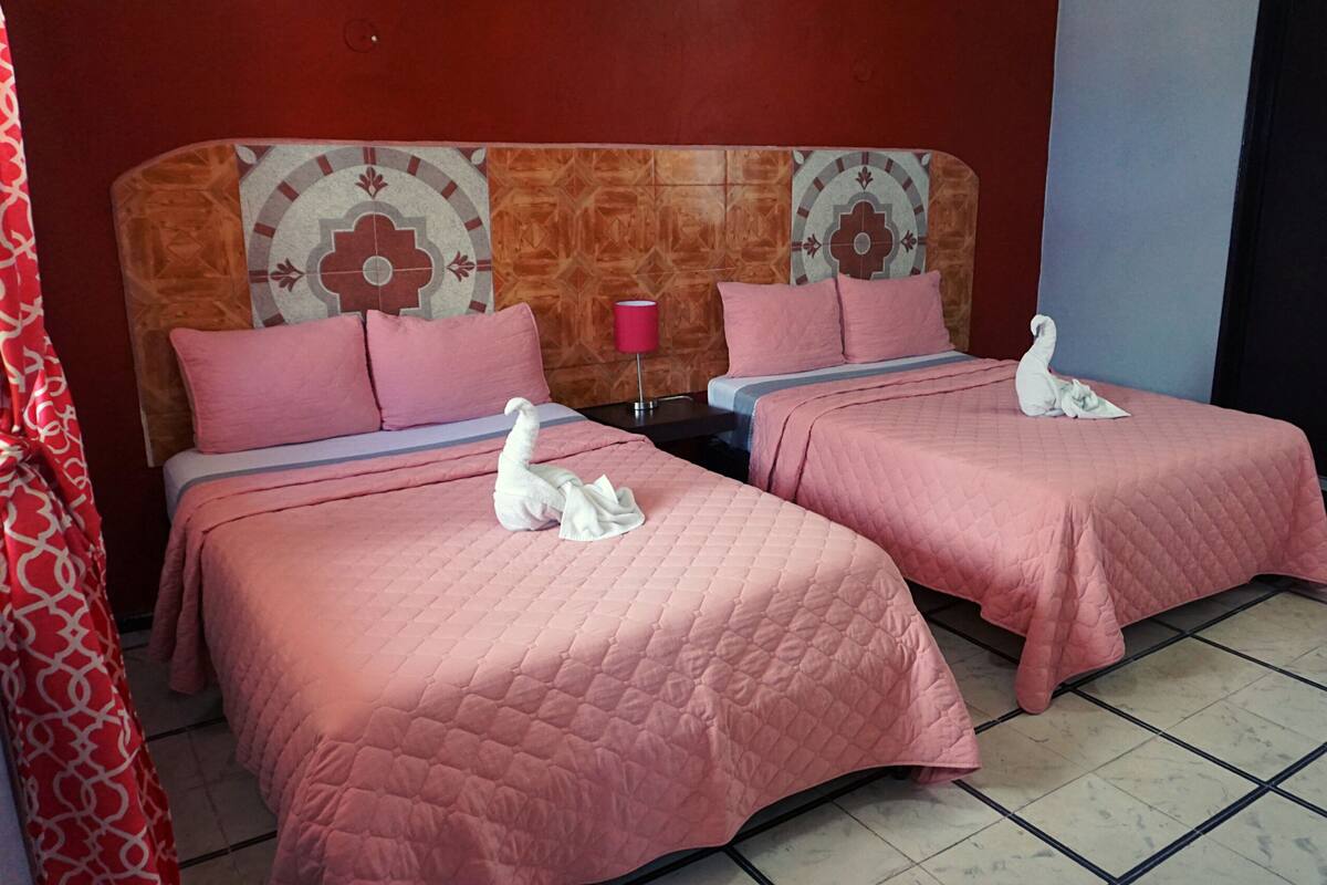 A hotel room with two beds, each with pink bedding and a swan-shaped towel.