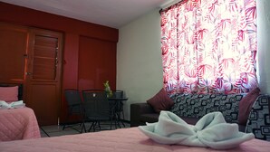Una habitación de hotel con una cama, una pequeña mesa con sillas, un sofá y un ventanal con cortinas estampadas.