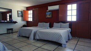 Una habitación con dos camas, una mesita, un espejo y una ventana con persianas.