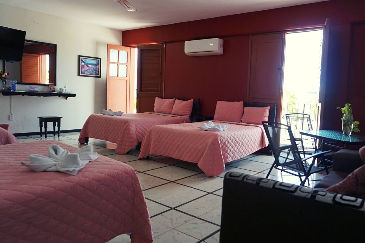 A hotel room with two beds, a small table, a chair, and a window with a view.