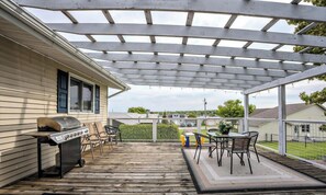 A covered patio with a grill, outdoor furniture, and a view of neighboring houses. - Hazel House steps from Boat Launch (Saint Ignace)