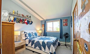 Un dormitorio con cama, escritorio, silla, ventilador y ventana.