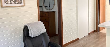Ett rum med en svart läderfåtölj, en byrå i trä, en vit tegelvägg och en dörr som leder till ett annat rum.
