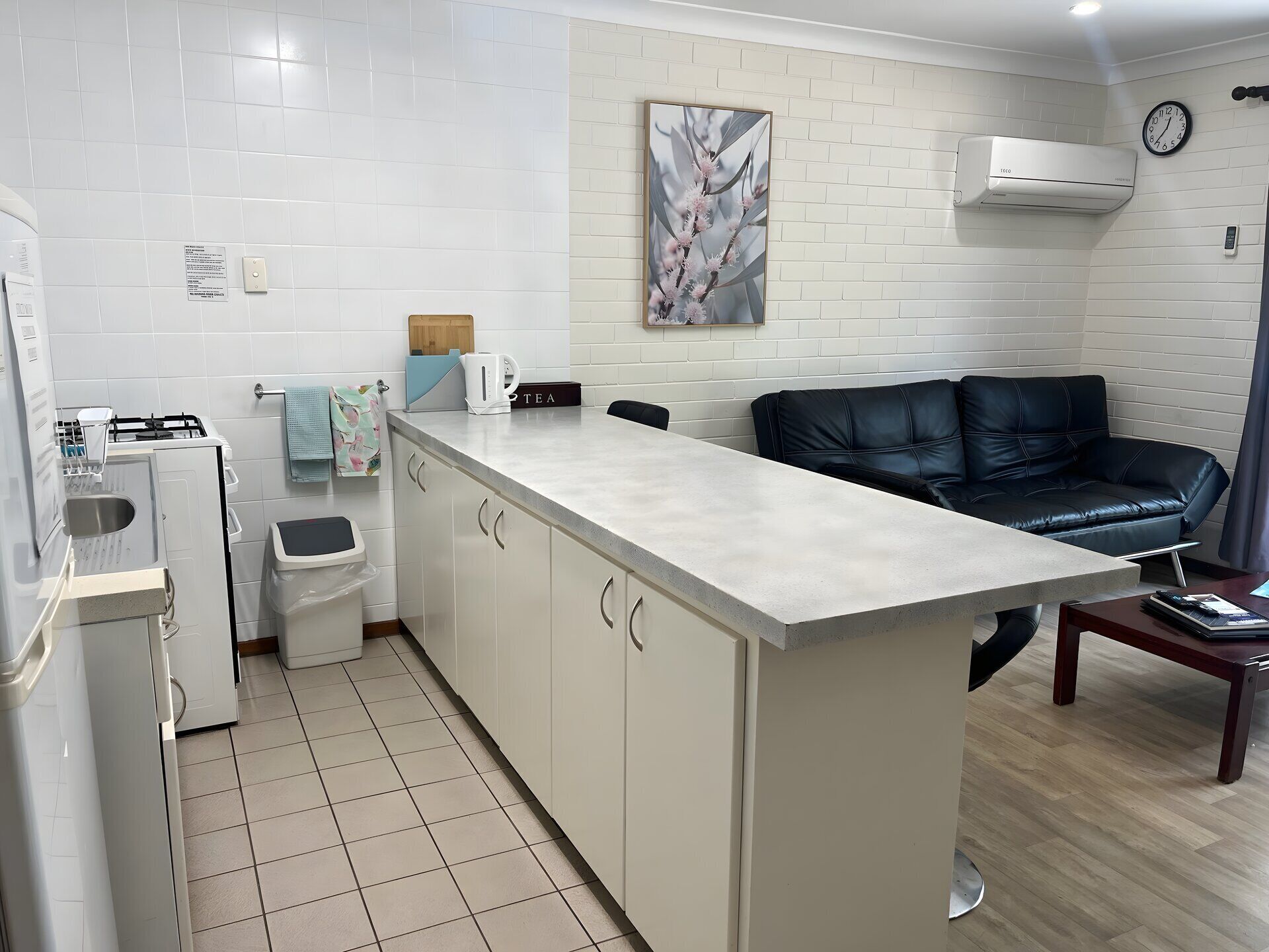 A compact kitchen with a built-in counter, a coffee machine, and a trash bin.