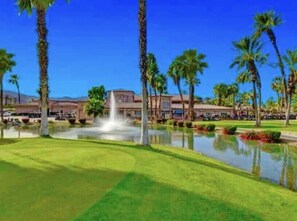 Ein Golfplatz mit Springbrunnen, Palmen und einem Gebäude im Hintergrund.