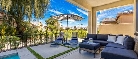A covered outdoor patio with a pool, lounge chairs, and a sofa.