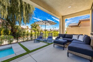 Eine überdachte Terrasse im Freien mit Pool, Liegestühlen und einer Couch.