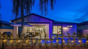 A modern house with a swimming pool, outdoor seating, and a well-lit patio area. - Walk to Coachella! Desert Paradise- with arcade games & Private Pool! (Indio)
