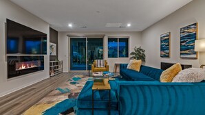 Uma sala de estar moderna com um sofá azul, uma lareira e uma janela grande com vista para uma paisagem urbana.