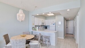 Une cuisine moderne avec des meubles blancs, un îlot central et un coin repas doté de chaises en osier.