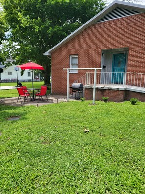 A brick building with a blue door, a barbecue grill, and a red umbrella over a table and chairs. - 1500 Sq.ft. of Quaint Comfort in the heart of Olney close to downtown! (Olney)
