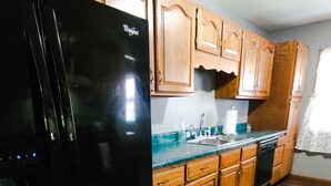 Una cocina con armarios de madera, un refrigerador Whirlpool negro, un lavavajillas y una encimera con un fregadero.