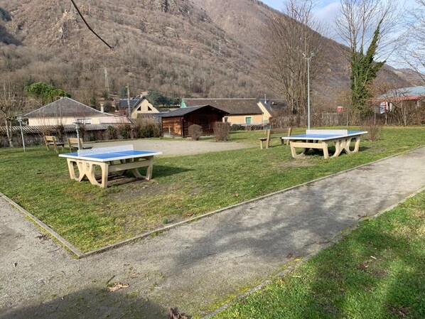 Un espacio al aire libre con dos mesas de ping pong, un camino de hormigón y un edificio al fondo.