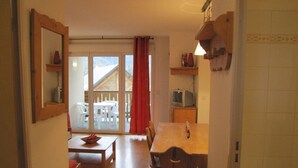 Un comedor con mesa y sillas de madera, una pequeña cocina con microondas y vistas a un balcón con sillas blancas.